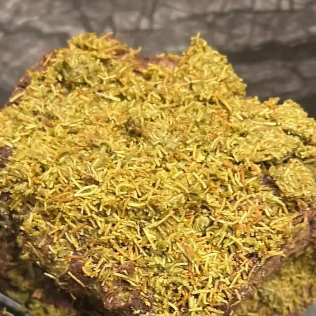 Close-up of a chocolate brownie covered in a thick layer of shredded pistachio kataifi.